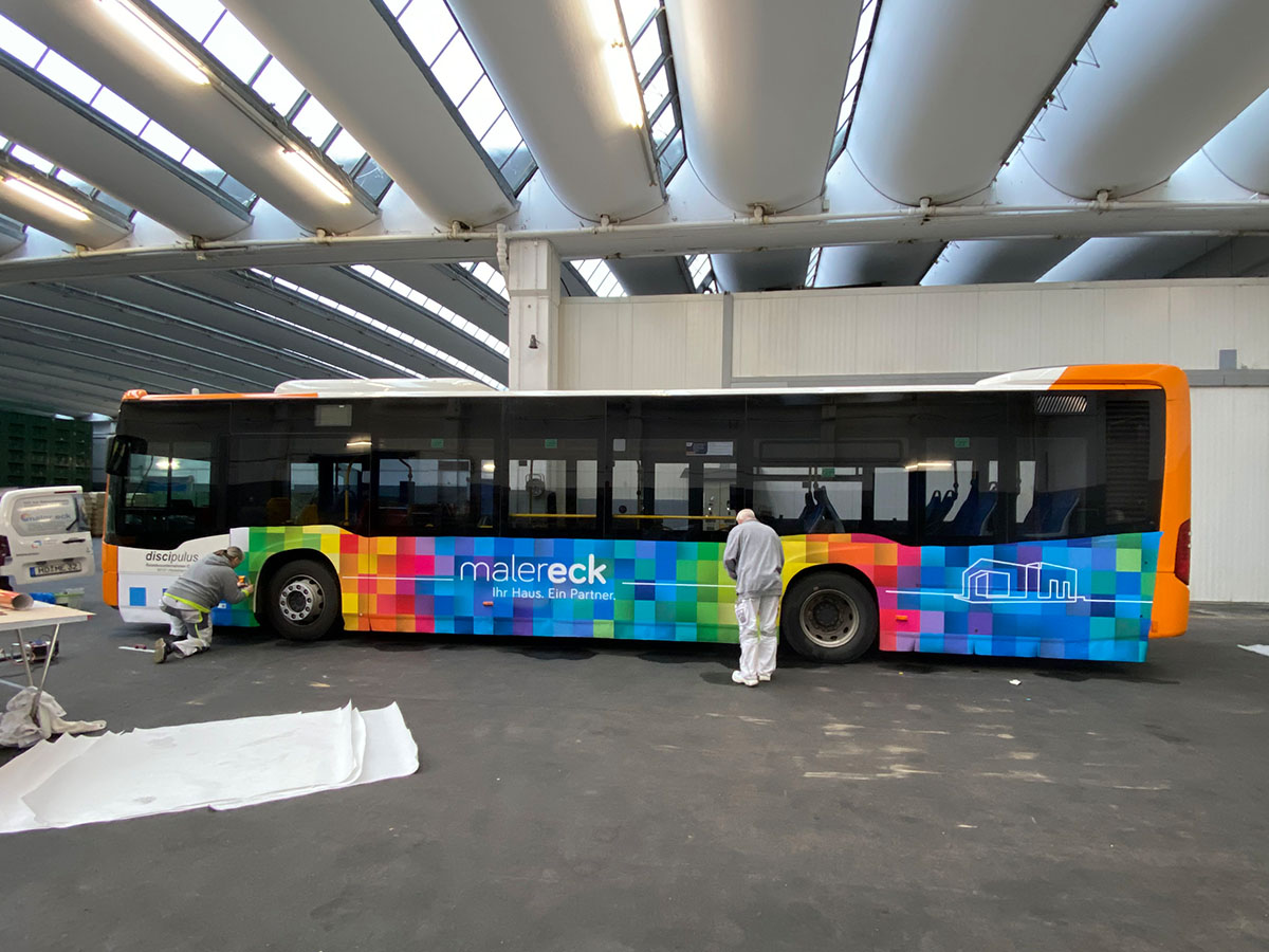 Bus mit bunter Beklebung von Maler Eck in Heidelberg, zwei Maler bei der Arbeit.