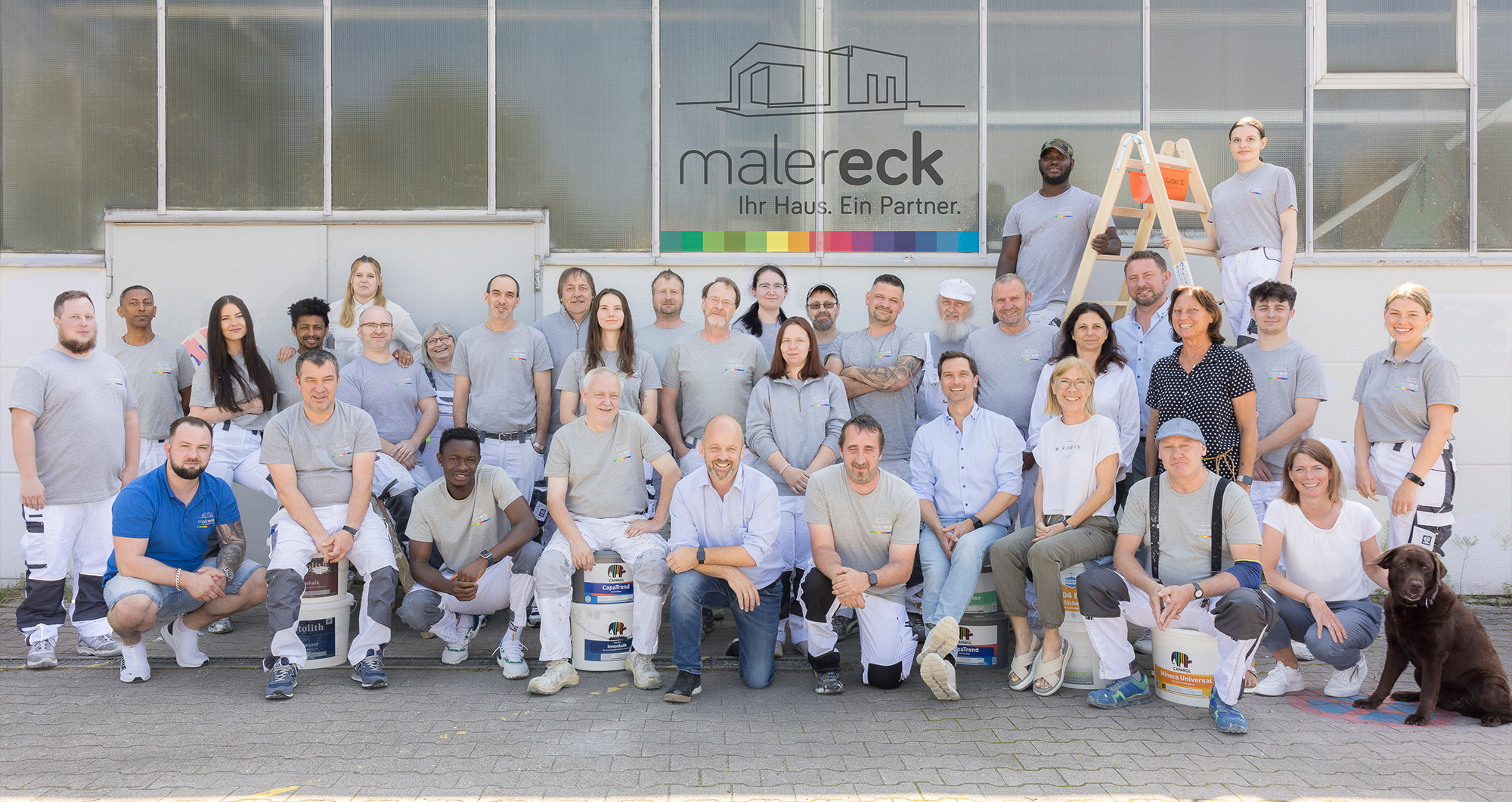 Team von Maler Eck in Heidelberg vor der Werkstatt, Malermeister und Mitarbeiter in Arbeitskleidung.